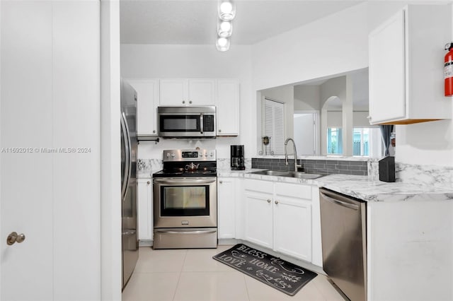 kitchen featuring light stone counters, stainless steel appliances, light tile patterned floors, sink, and white cabinets