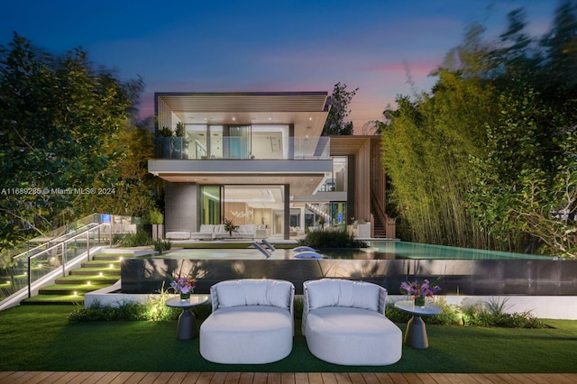 back house at dusk with outdoor lounge area and a balcony