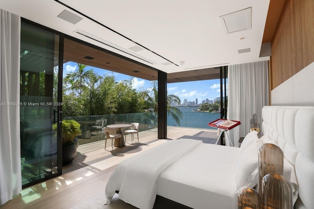 bedroom featuring expansive windows, light wood-type flooring, a water view, and wooden walls