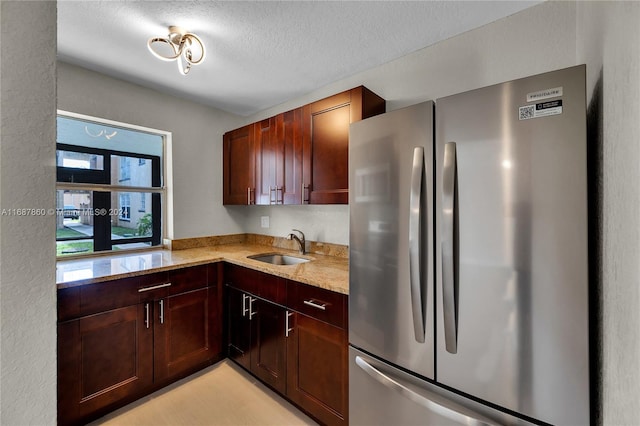 kitchen featuring a textured ceiling, sink, stainless steel refrigerator, and light stone countertops