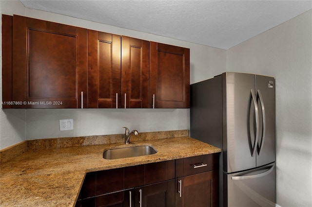 kitchen featuring light stone counters, sink, stainless steel refrigerator, and a textured ceiling