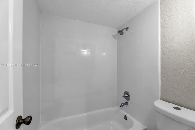 bathroom featuring a textured ceiling, toilet, and tiled shower / bath combo