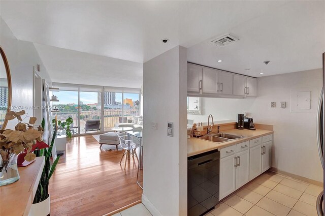 kitchen featuring white cabinets, sink, light tile patterned floors, and black dishwasher