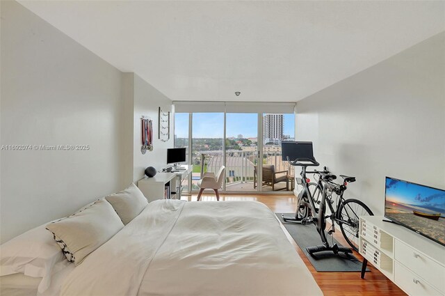 bedroom with access to outside, hardwood / wood-style flooring, and a wall of windows