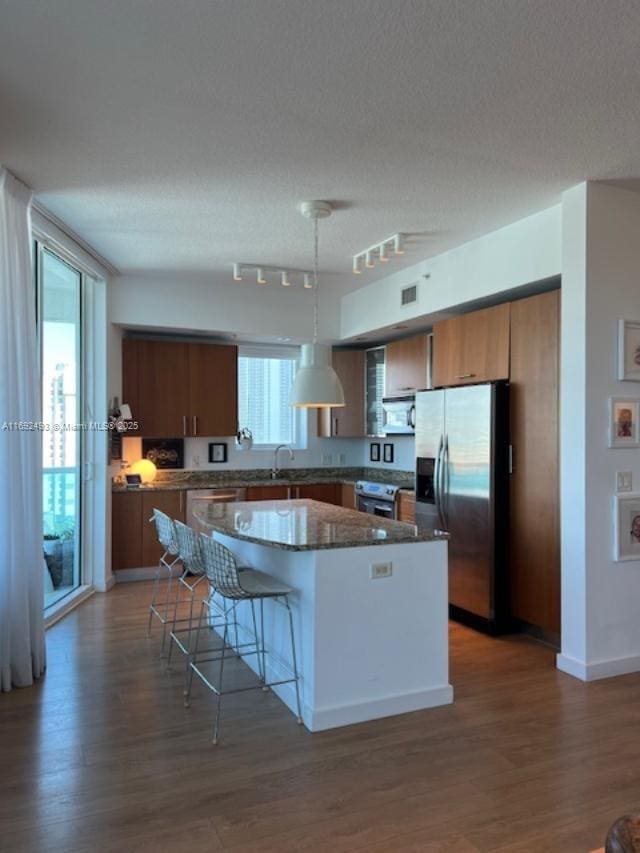 kitchen featuring wood finished floors, a center island, stainless steel appliances, a kitchen bar, and a sink