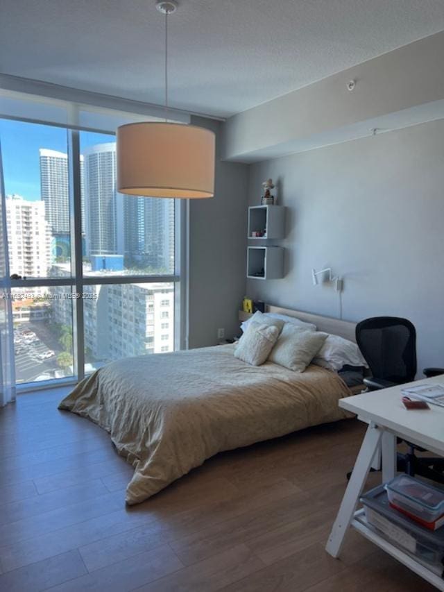 bedroom featuring a view of city, a wall of windows, and wood finished floors