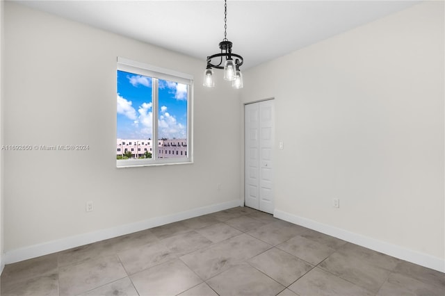 tiled spare room featuring an inviting chandelier