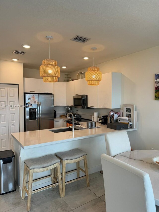 kitchen featuring kitchen peninsula, white cabinetry, pendant lighting, and appliances with stainless steel finishes