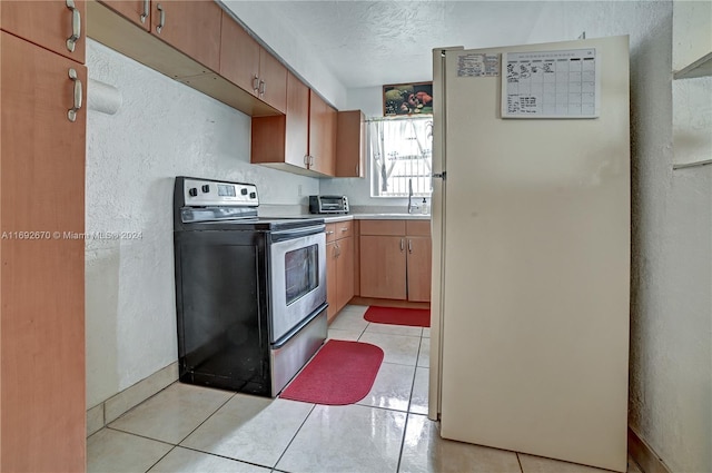 kitchen with light tile patterned floors, a textured ceiling, stainless steel range with electric stovetop, and white fridge