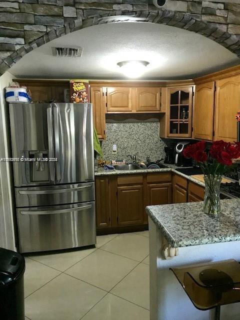 kitchen featuring sink, light stone countertops, light tile patterned floors, stainless steel fridge, and decorative backsplash