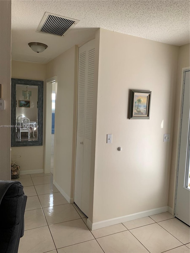 corridor featuring a textured ceiling and light tile patterned floors