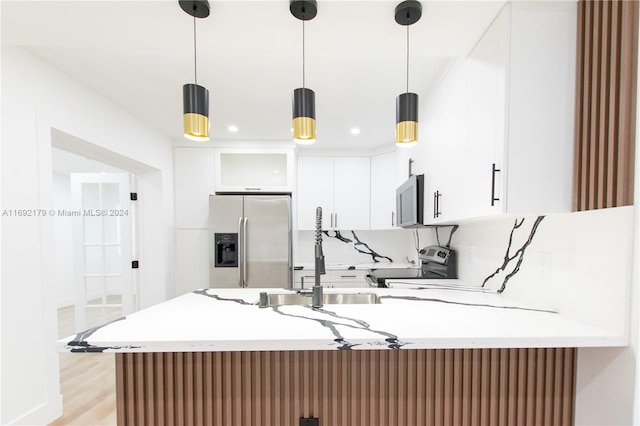 kitchen featuring white cabinets, appliances with stainless steel finishes, hanging light fixtures, and light hardwood / wood-style floors