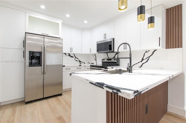 kitchen featuring white cabinetry, appliances with stainless steel finishes, hanging light fixtures, kitchen peninsula, and light hardwood / wood-style flooring