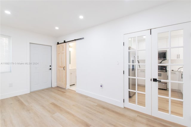 spare room featuring a barn door, light wood-type flooring, and french doors