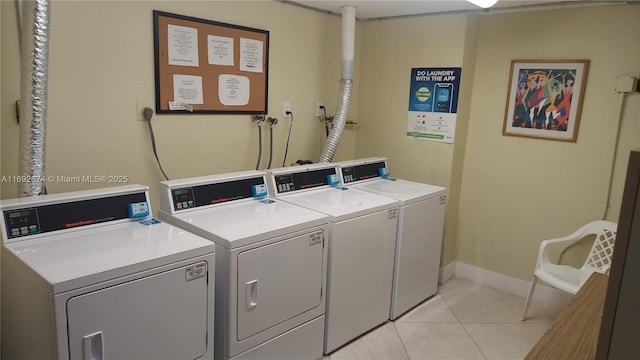 shared laundry area featuring light tile patterned flooring, washing machine and clothes dryer, and baseboards