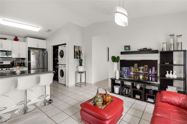 tiled living room with a textured ceiling, stacked washer and dryer, and lofted ceiling