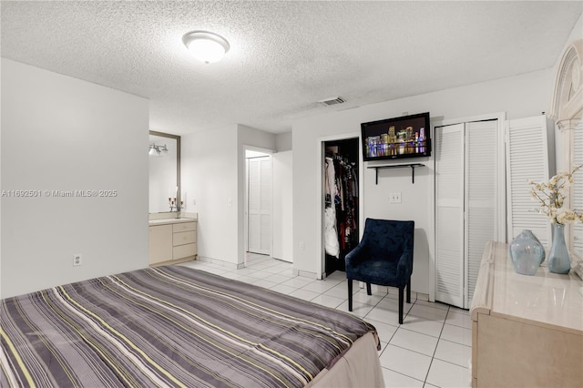 bedroom featuring ensuite bathroom, light tile patterned floors, and a textured ceiling