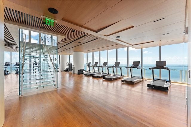 workout area with light wood-type flooring, a wall of windows, a water view, and wooden ceiling