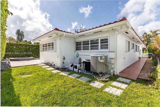 back of property featuring a yard, a tiled roof, central AC unit, and stucco siding