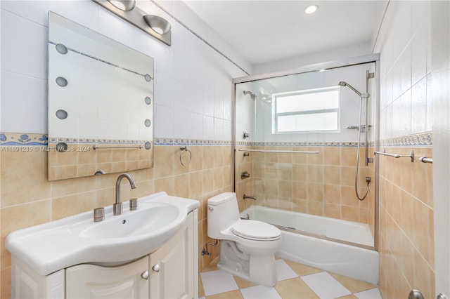 full bathroom featuring shower / bath combination with glass door, vanity, toilet, and tile walls