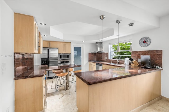 kitchen with a peninsula, light brown cabinetry, a raised ceiling, a sink, and appliances with stainless steel finishes