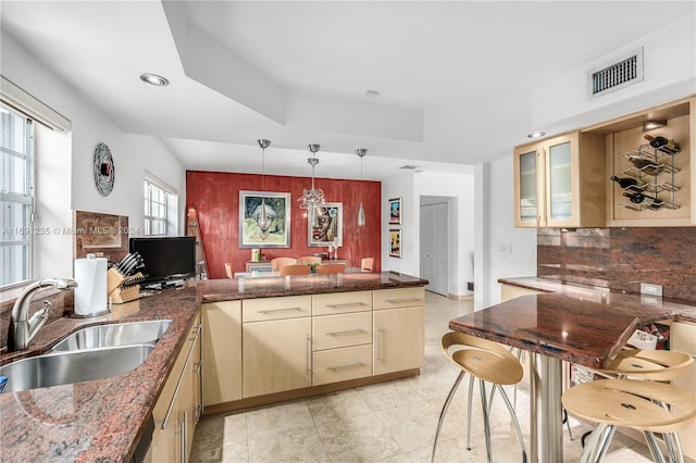 kitchen with pendant lighting, light brown cabinets, backsplash, sink, and kitchen peninsula