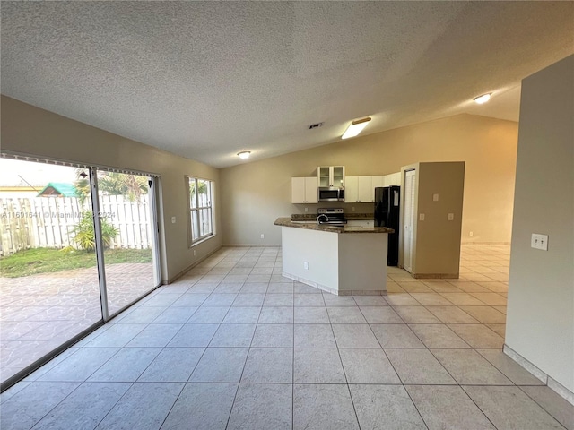 kitchen featuring appliances with stainless steel finishes, a textured ceiling, light tile patterned floors, white cabinets, and vaulted ceiling