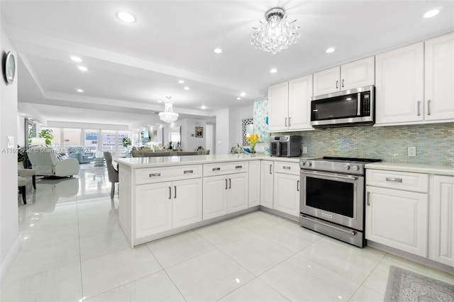 kitchen featuring stainless steel appliances, white cabinetry, kitchen peninsula, backsplash, and a notable chandelier