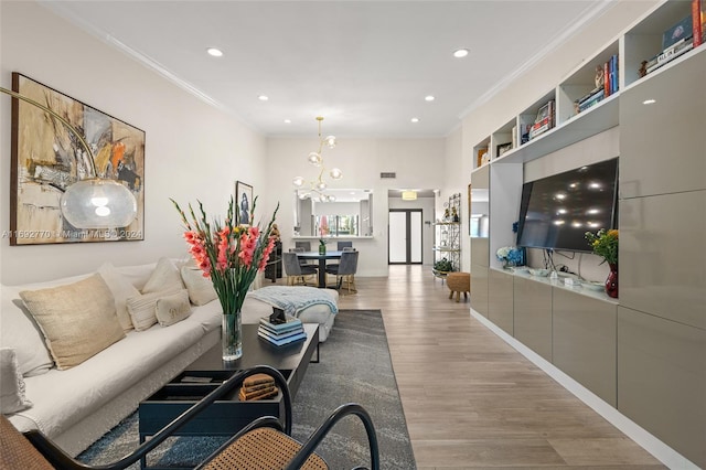 living room with built in shelves, a chandelier, light hardwood / wood-style floors, and crown molding