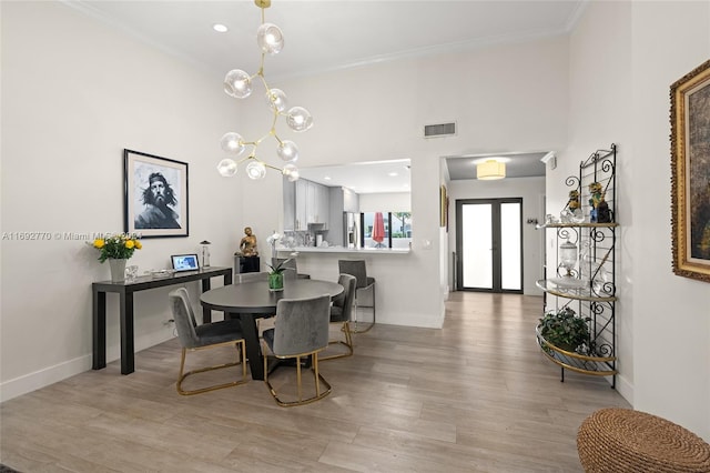 dining area featuring french doors, light wood-type flooring, a notable chandelier, and crown molding