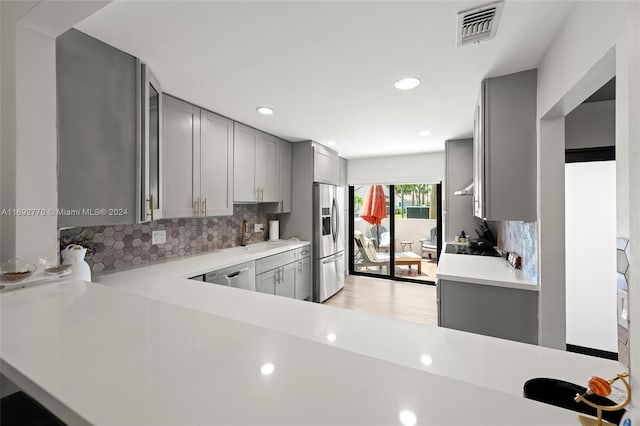 kitchen featuring stainless steel appliances, sink, kitchen peninsula, backsplash, and gray cabinetry