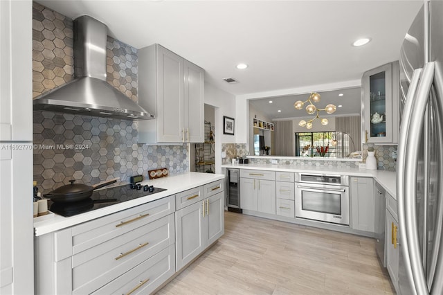 kitchen featuring stainless steel appliances, wall chimney exhaust hood, light wood-type flooring, and backsplash