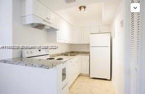 kitchen featuring white cabinetry, kitchen peninsula, exhaust hood, light stone countertops, and white appliances