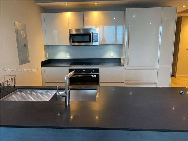 kitchen featuring electric panel, sink, oven, black stovetop, and light hardwood / wood-style flooring