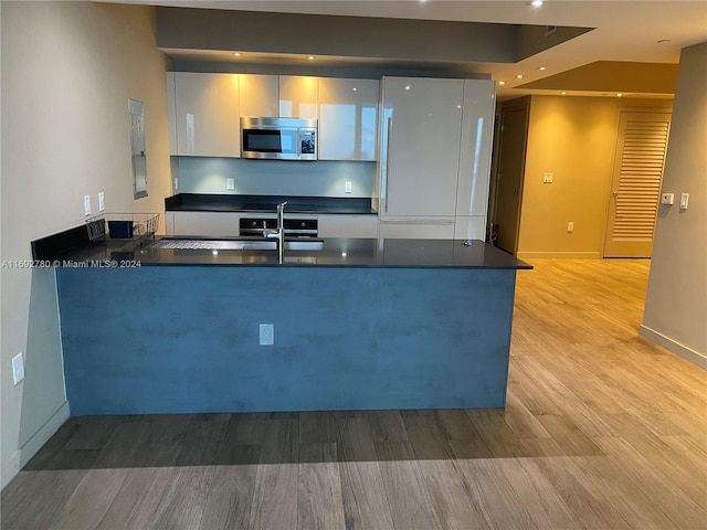 kitchen featuring white cabinets, kitchen peninsula, sink, and light wood-type flooring