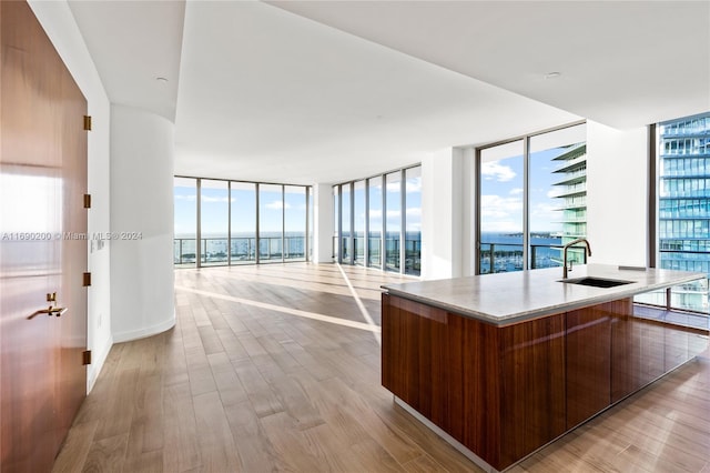 kitchen with a kitchen island with sink, expansive windows, a water view, sink, and light hardwood / wood-style floors