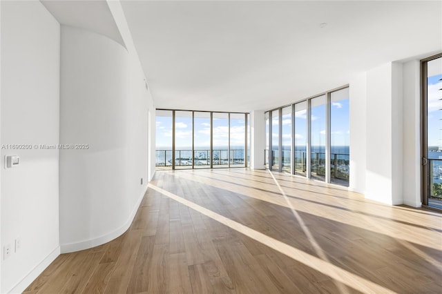 empty room with expansive windows, baseboards, wood finished floors, and a water view