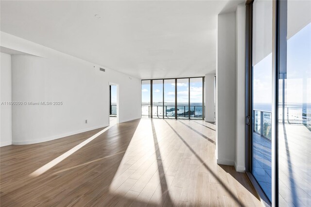 spare room with floor to ceiling windows, hardwood / wood-style floors, and a water view