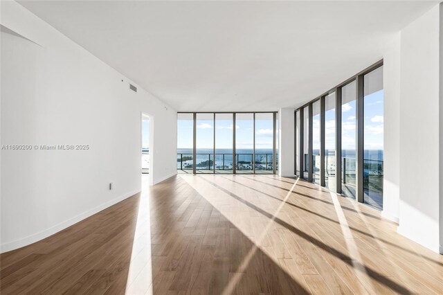 unfurnished room featuring a water view, a wall of windows, and wood-type flooring