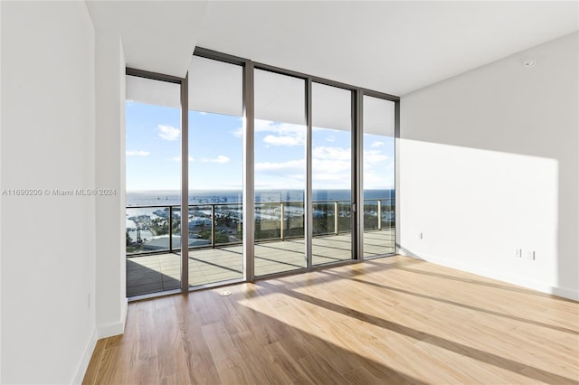 spare room with a water view, light hardwood / wood-style flooring, and expansive windows