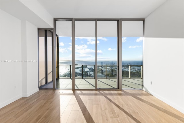 empty room with floor to ceiling windows, a water view, and wood-type flooring