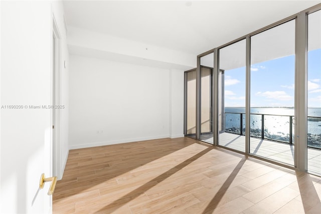 spare room featuring light wood finished floors, a water view, baseboards, and expansive windows