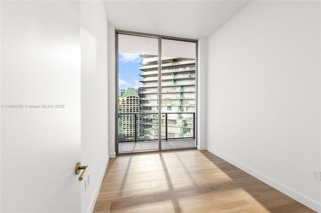 empty room with a view of city, floor to ceiling windows, wood finished floors, and baseboards