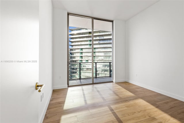 unfurnished room with a wall of windows, baseboards, and wood finished floors