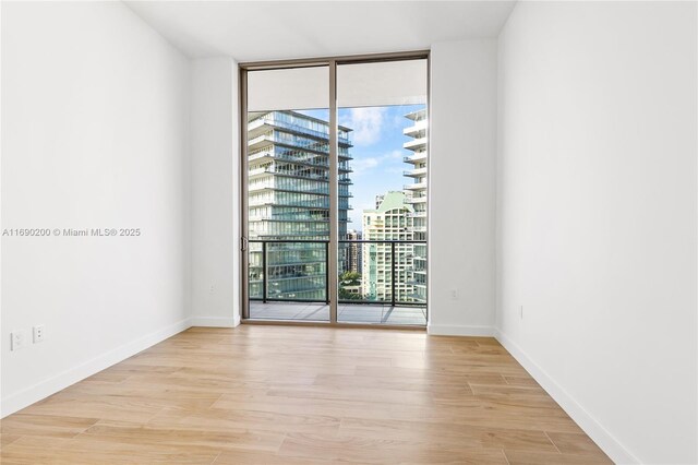 empty room with floor to ceiling windows and light wood-type flooring