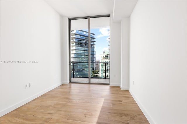 spare room with baseboards, light wood-style flooring, floor to ceiling windows, and a view of city