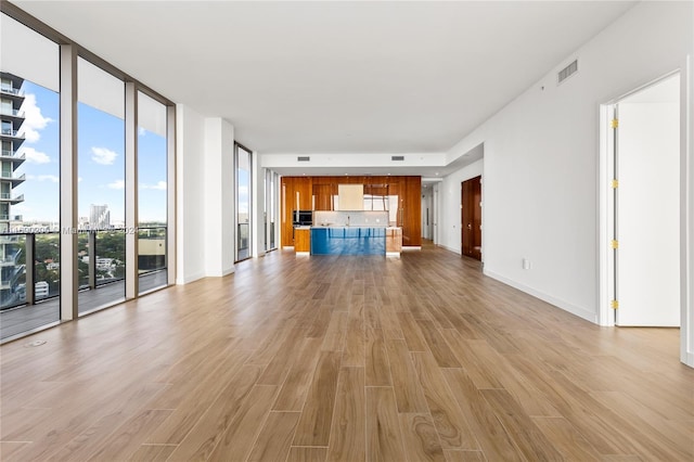 unfurnished living room with floor to ceiling windows, a healthy amount of sunlight, and light hardwood / wood-style floors