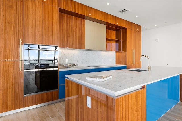 kitchen with a kitchen island with sink, black appliances, sink, light hardwood / wood-style flooring, and decorative backsplash