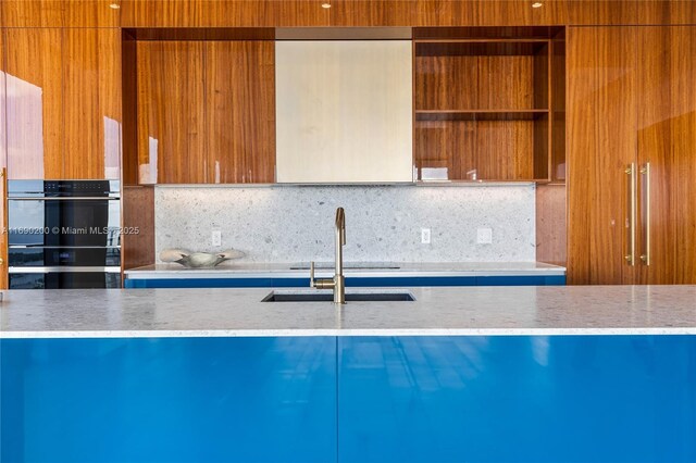 kitchen featuring backsplash, light stone countertops, sink, and stainless steel double oven