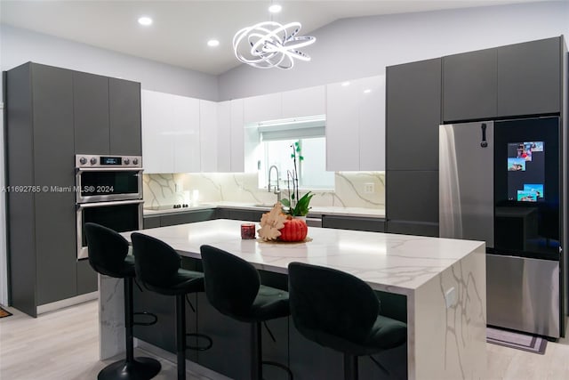 kitchen featuring stainless steel appliances, a kitchen island, decorative light fixtures, light hardwood / wood-style floors, and lofted ceiling